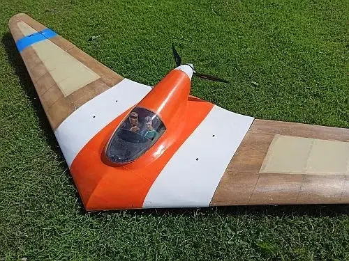 A small orange and white plane sitting on top of grass.