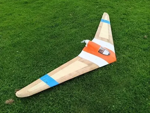 A wooden airplane is laying on the grass.